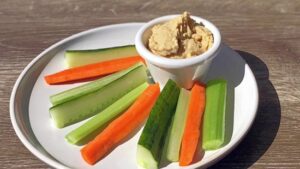 "A colorful assortment of carrot sticks, cucumber slices, and bell pepper strips served with a creamy hummus dip, combining crunchy veggies rich in vitamins and fiber with protein-packed, flavorful hummus."