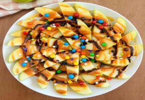 "Thin apple slices drizzled with almond or peanut butter, topped with granola, raisins, and a sprinkle of cinnamon, combining natural sugars, healthy fats, and a touch of crunch for a delightful snack."